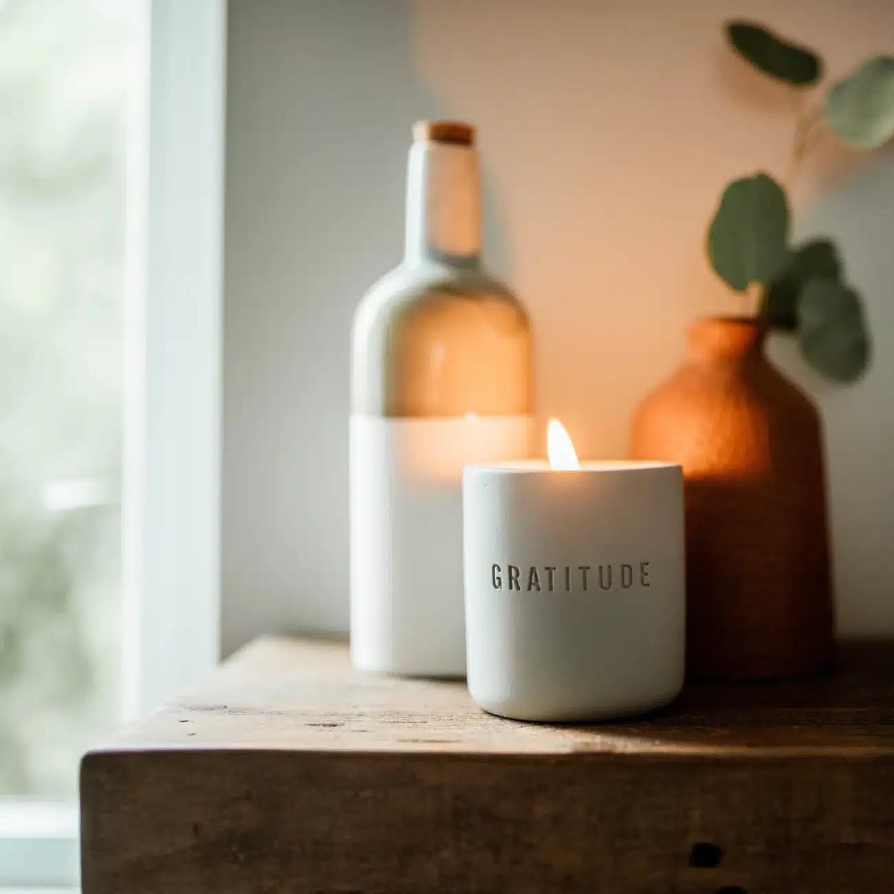 gratitude candle 3 Lit gratitude candle on a table in front of a bottle and vase