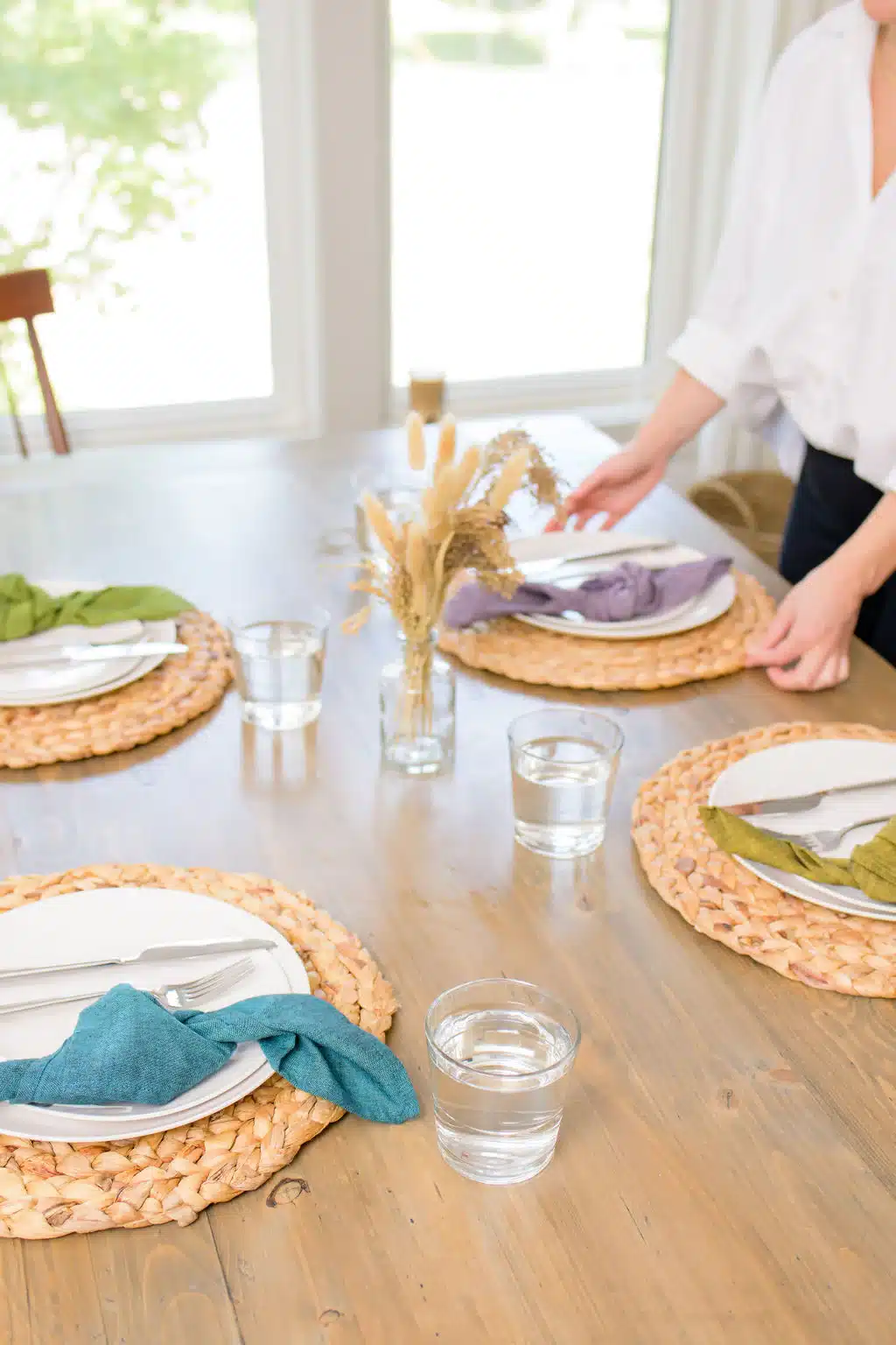SustainableThreadsLifestyle someone setting a wooden table with plates and various colored napkins