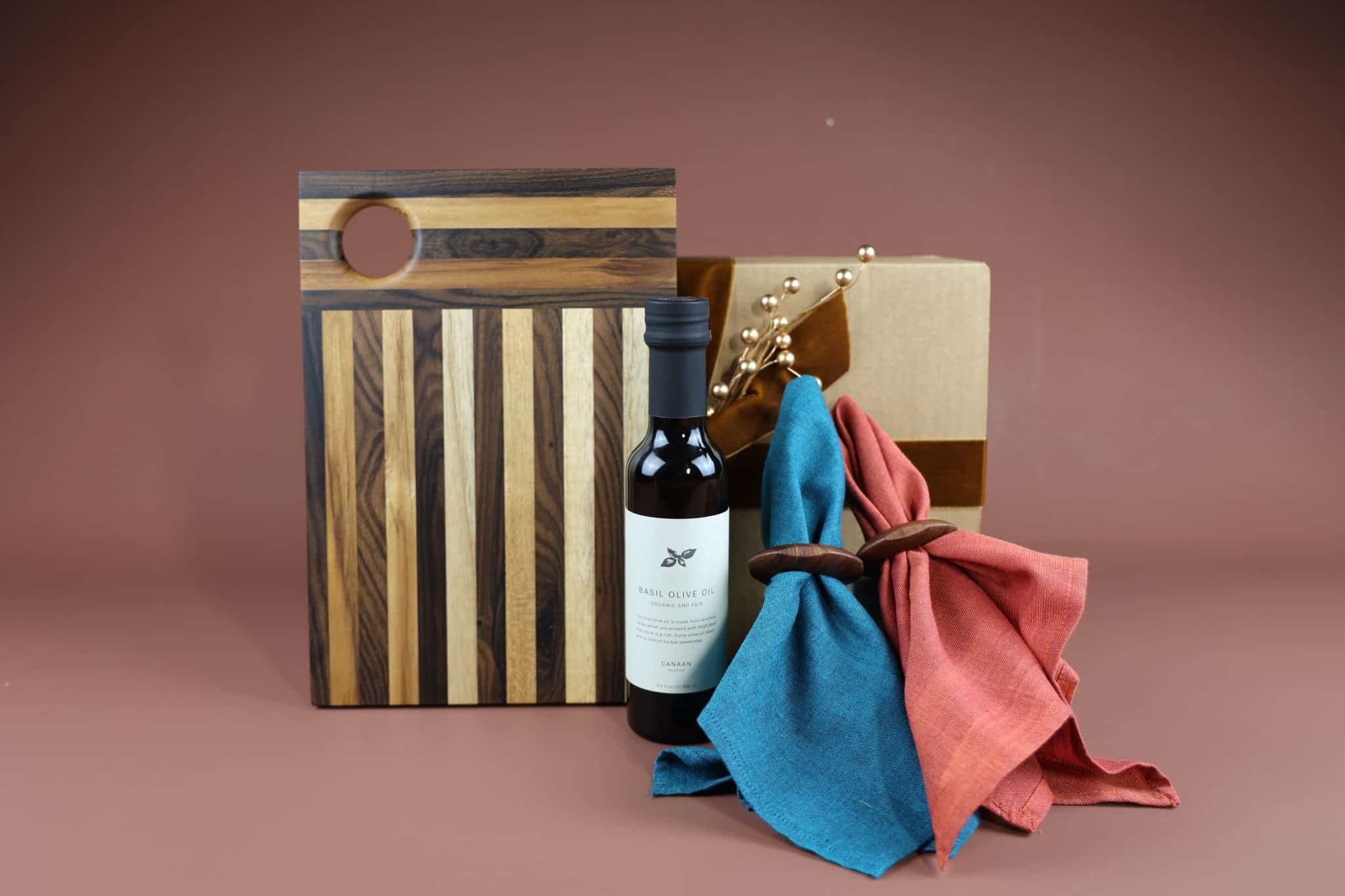 Gourment Goodness 2025 A holiday gift set featuring a mixed wood cutting board, olive oil, sustainably made napkins and wooden napkin rings