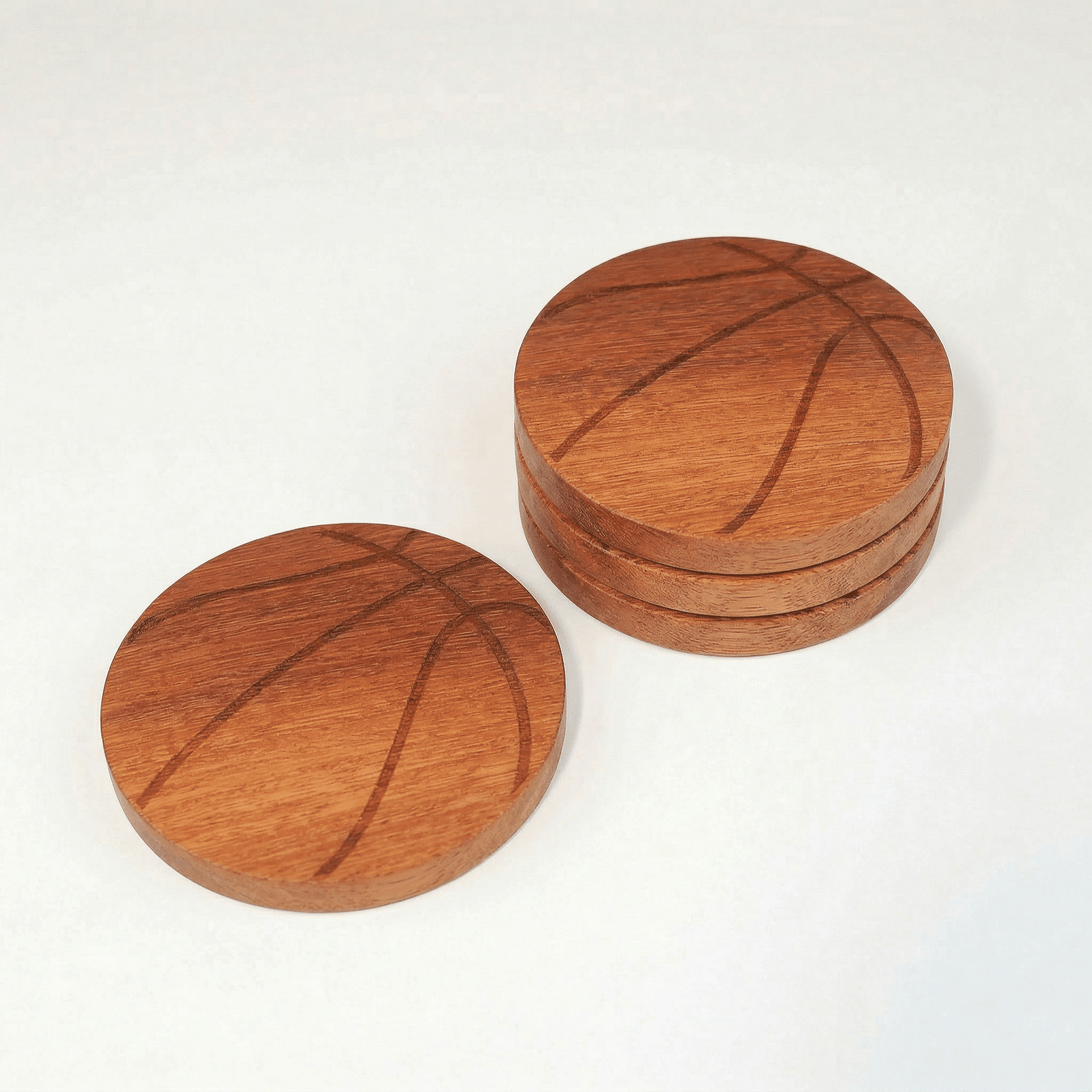 itza wood basketball coasters one coaster engraved to look like a basketball sits next to a stack of three of the same coaster