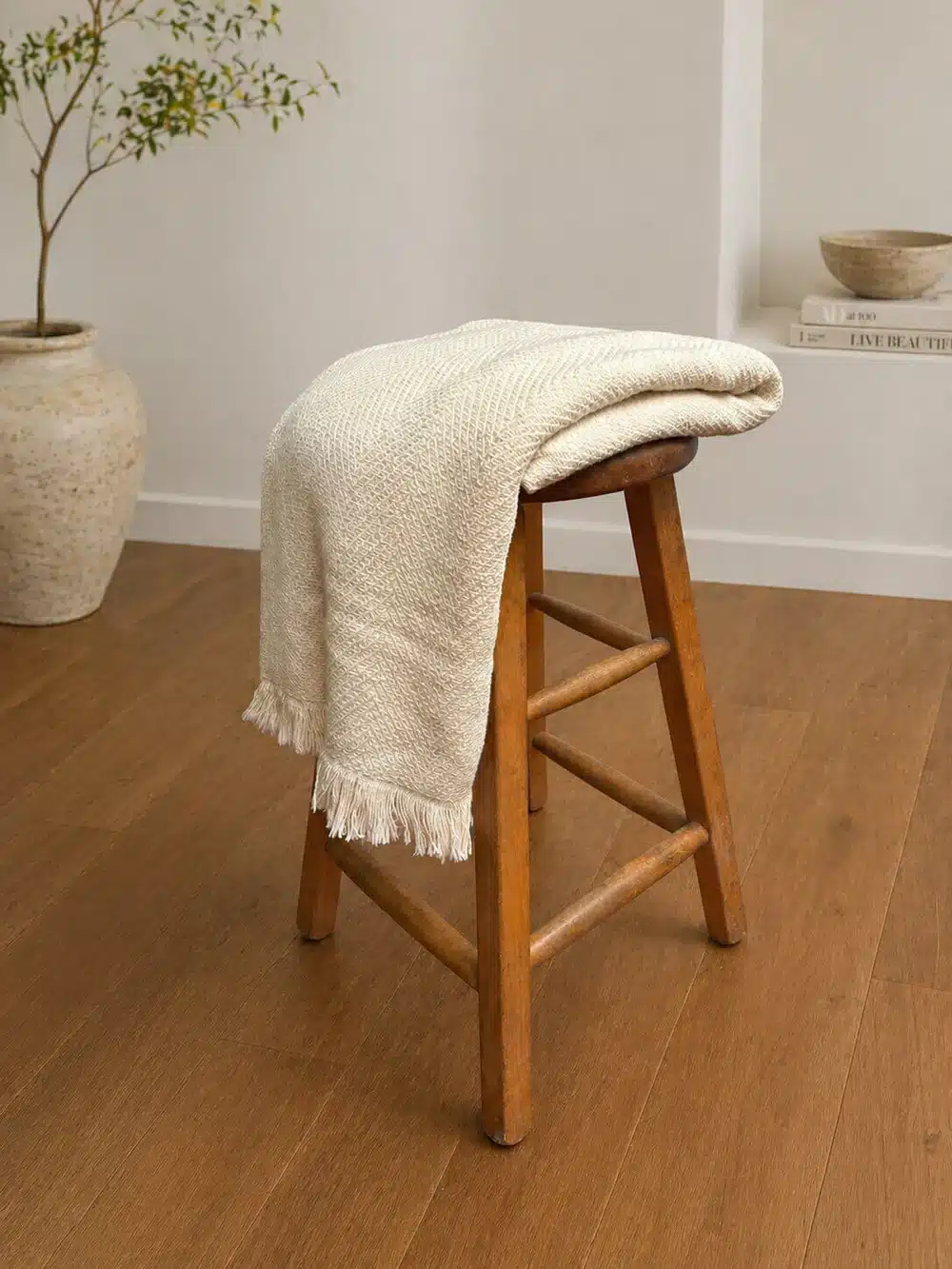 S&A american made blanket in natural - lifestyle a luxurious cream colored blanket is folded across a wooden stool