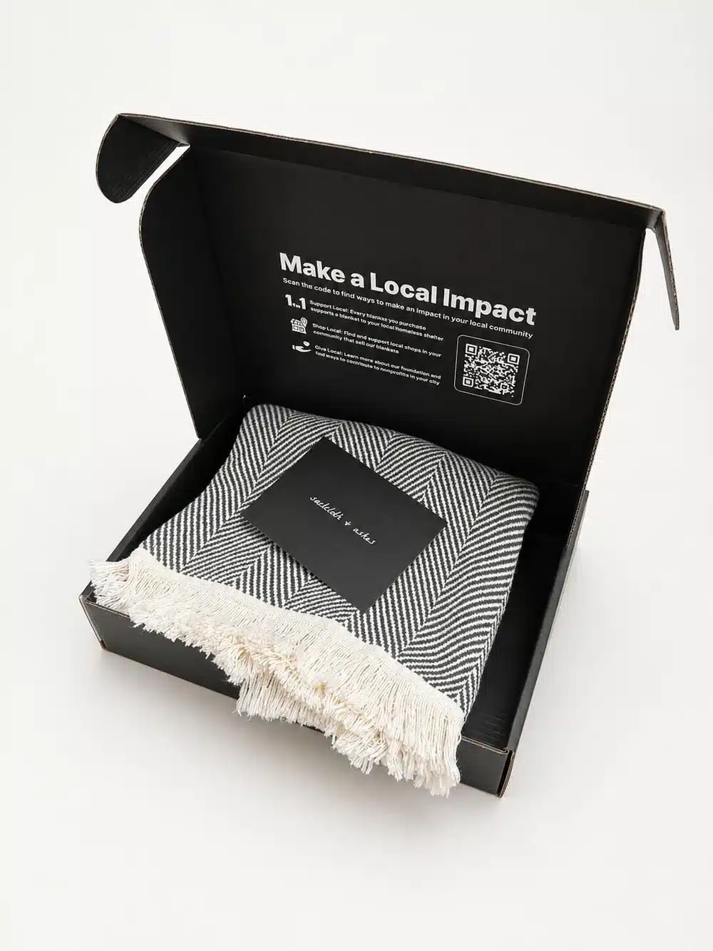 American Made S&A blanket in a box A luxurious grey and white herringbone blanket sits folded inside an opened box that says "make a local impact"