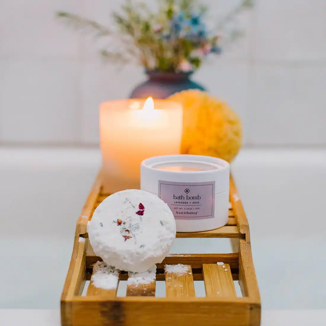 NH CB ThistleFarms bath bomb 274 1100x A lavender bath bomb placed next to a candle in a serene setting - a great item to add to a wellness gift for employees