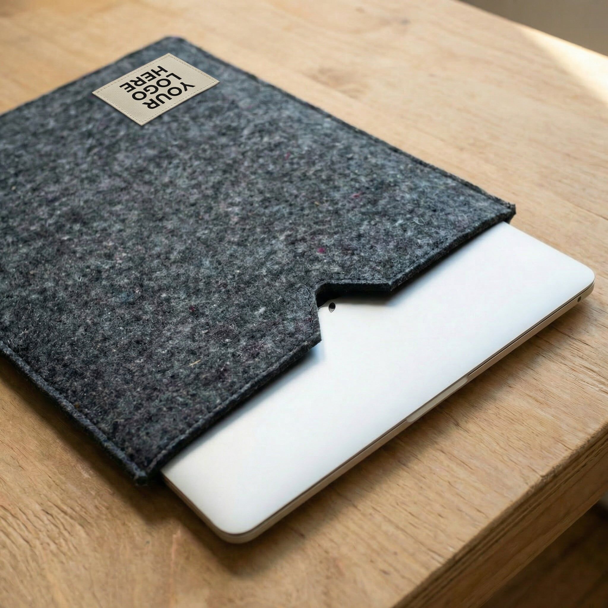 Good Felt Laptop sleeve vertical orientation AI A gray laptop sleeve made from recycled textile waste pictured on top of a desk with a laptop slid partway out of the sleeve