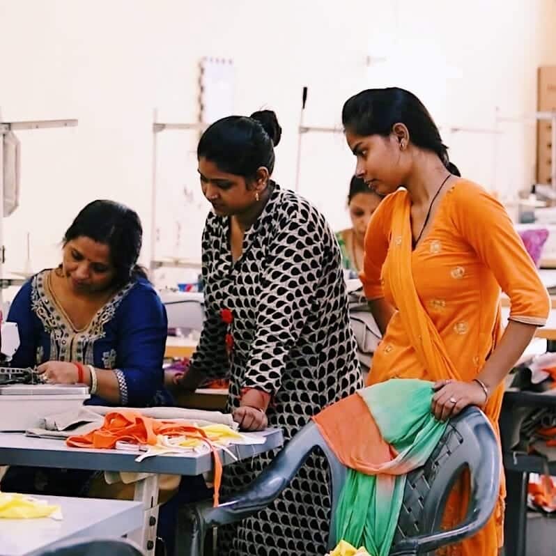 A woman sits at her sewing machine while two coworkers look over her shoulder A woman sits at her sewing machine while two coworkers look over her shoulder