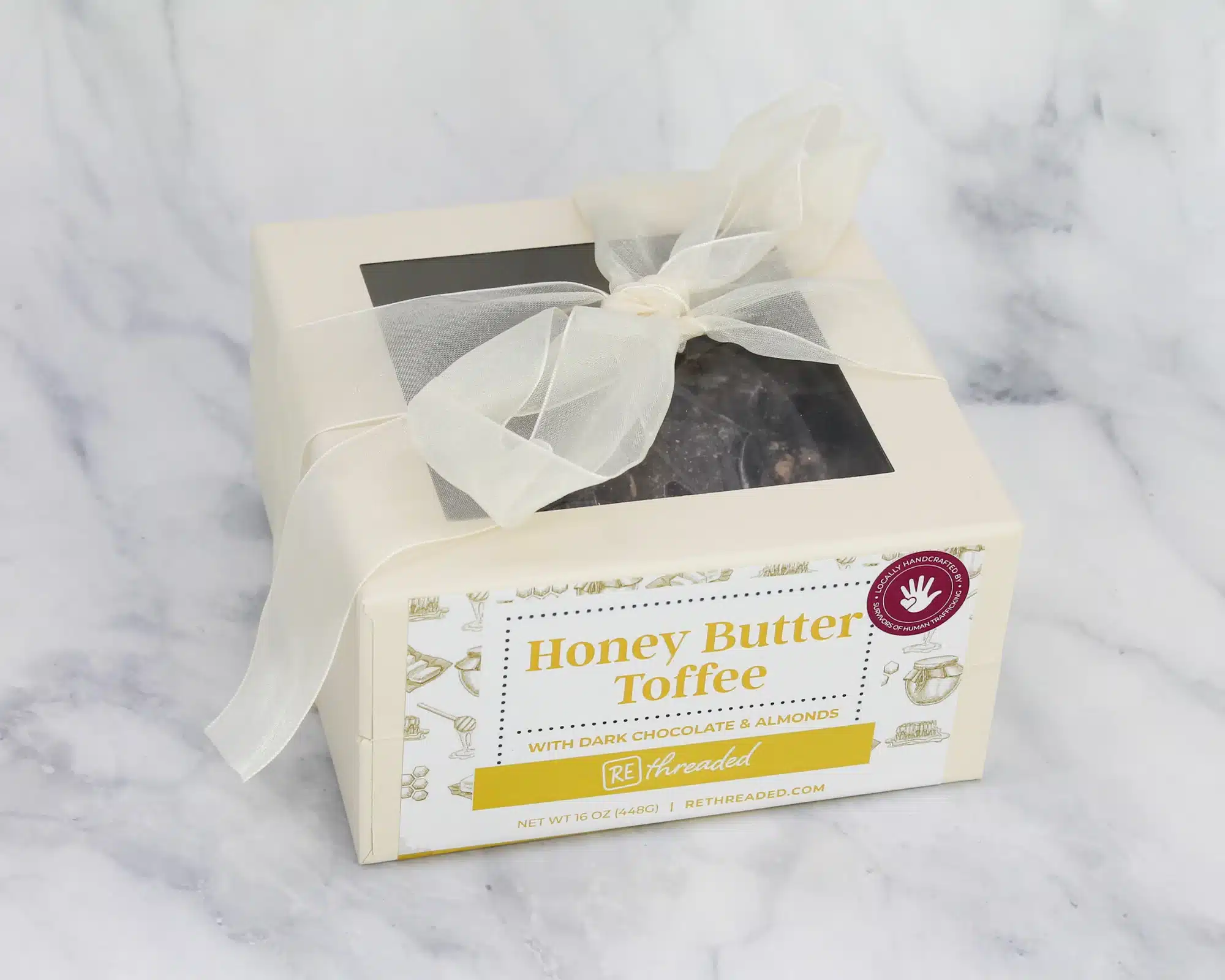 Rethreaded 1lb box toffee A box of Honey Butter Toffee with a white bow wrapped around it sits on a marble countertop